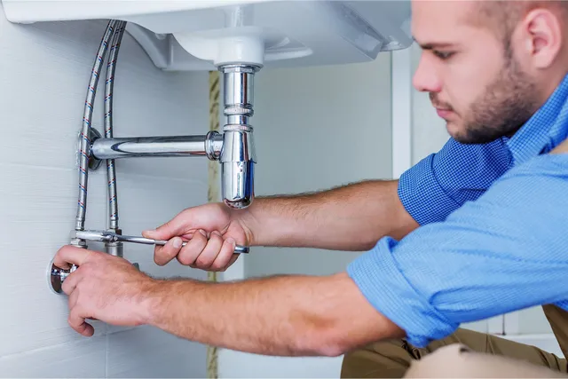 Plumber fixing sink pipes with wrench under bathroom sink