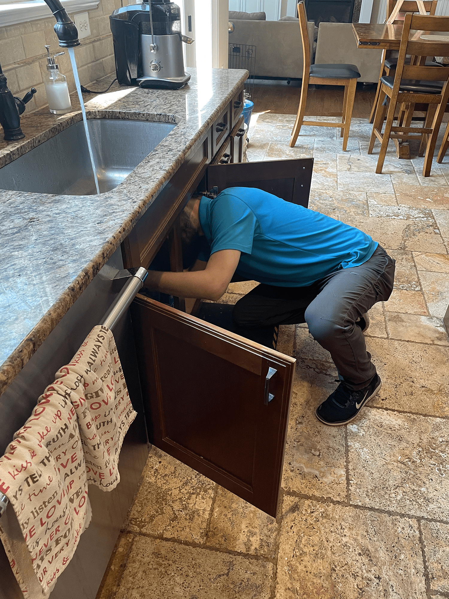 Person in blue shirt bending under kitchen sink, possibly fixing plumbing