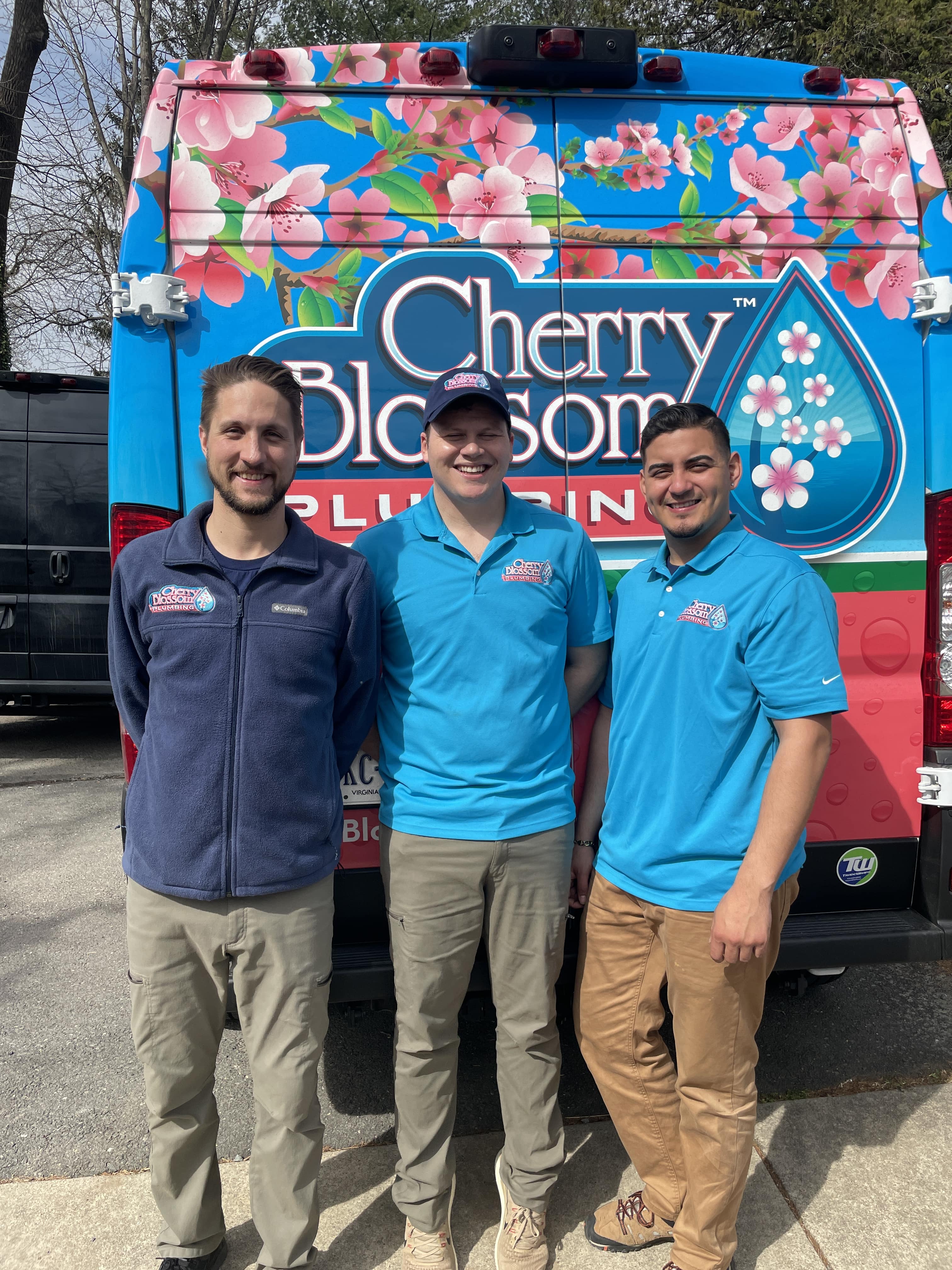 Three Cherry Blossom employees standing in front of floral-decorated company van