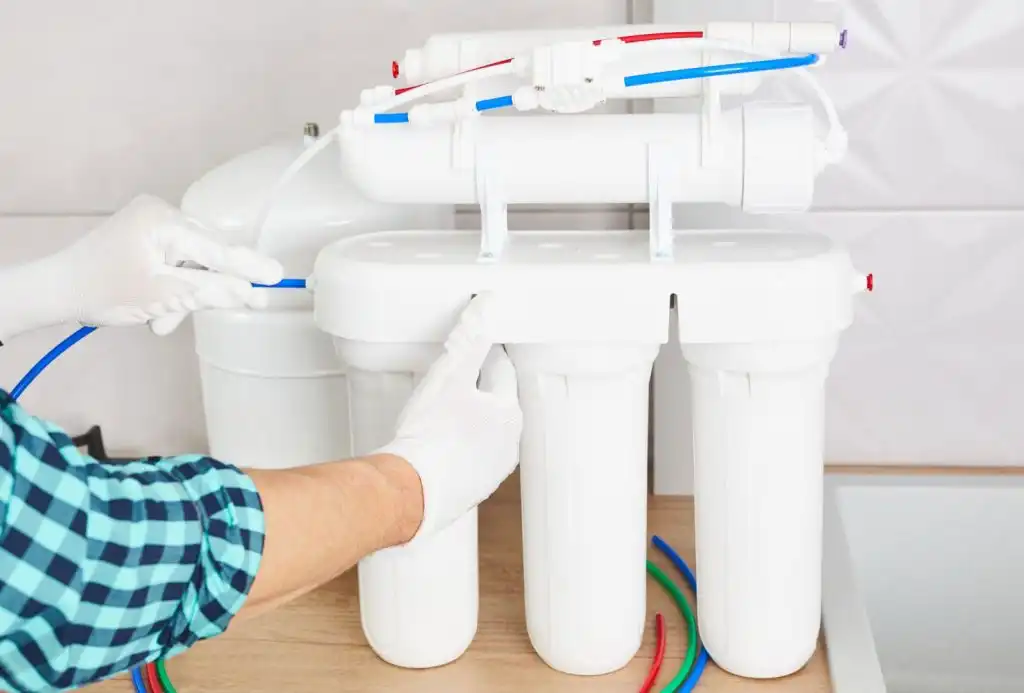 Person installing multi-stage water filtration system with white filter cartridges