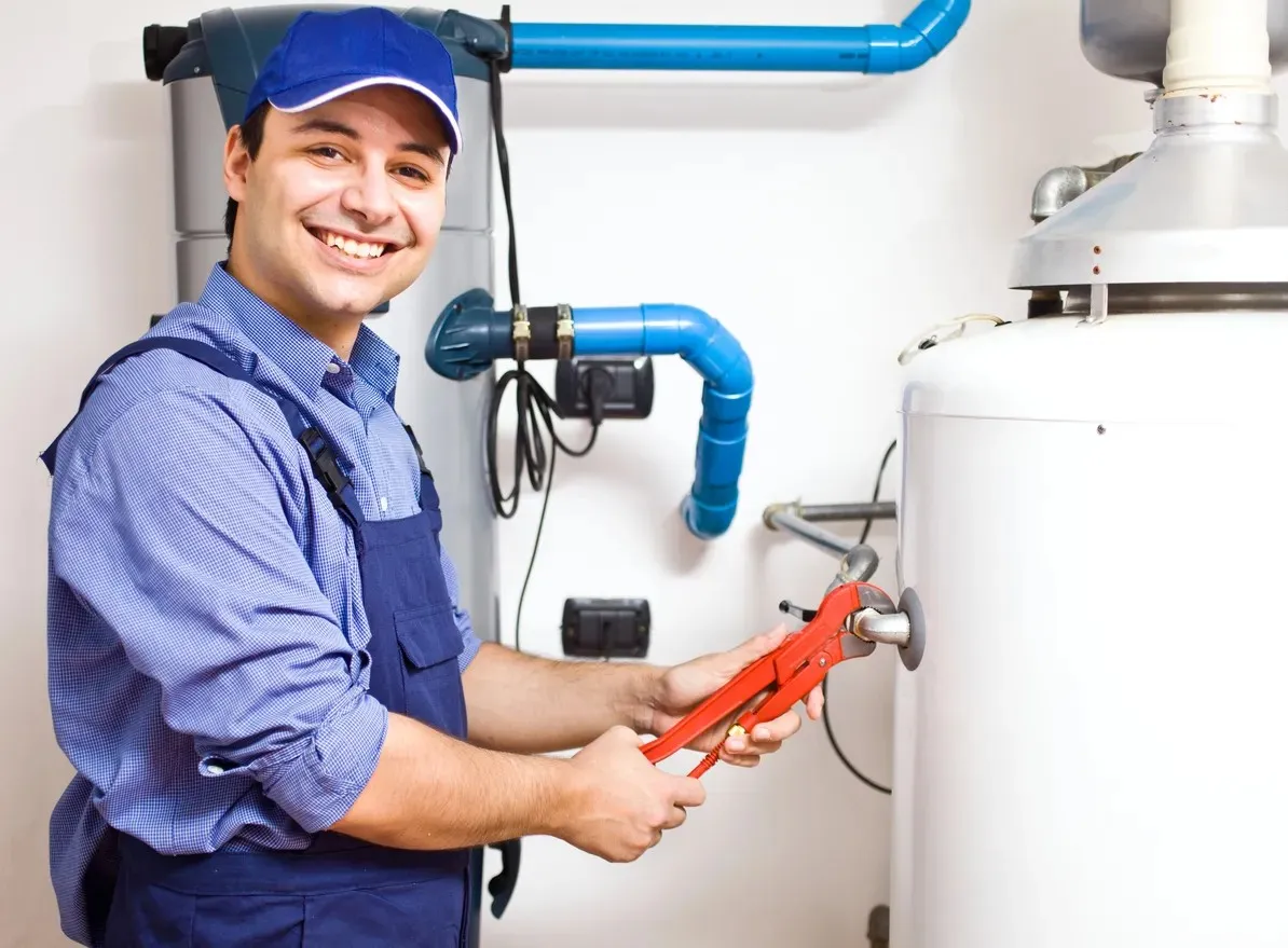 Smiling plumber in blue uniform fixing water heater with red wrench