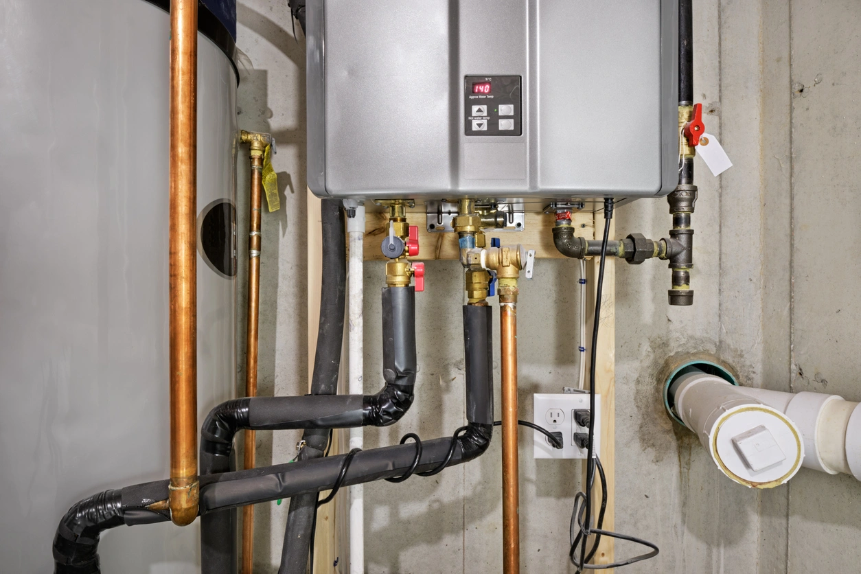 Tankless water heater and piping system on a concrete wall. Copper pipes, valves, and insulated sections emphasize efficiency and modern utility setup.