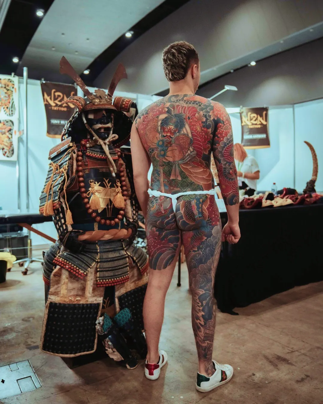 Expo attendee showing full back tattoo design in front of a samurai display at the Australian Tattoo Expo