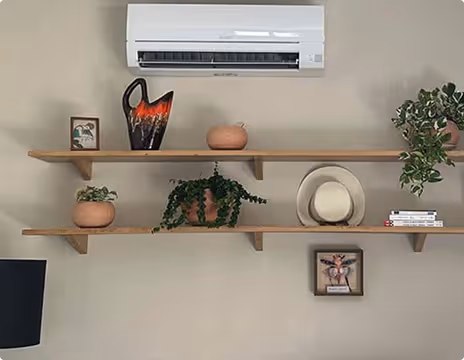 Deux étagères murales en bois avec des plantes en pots, des décorations et un climatiseur blanc fixé en haut.