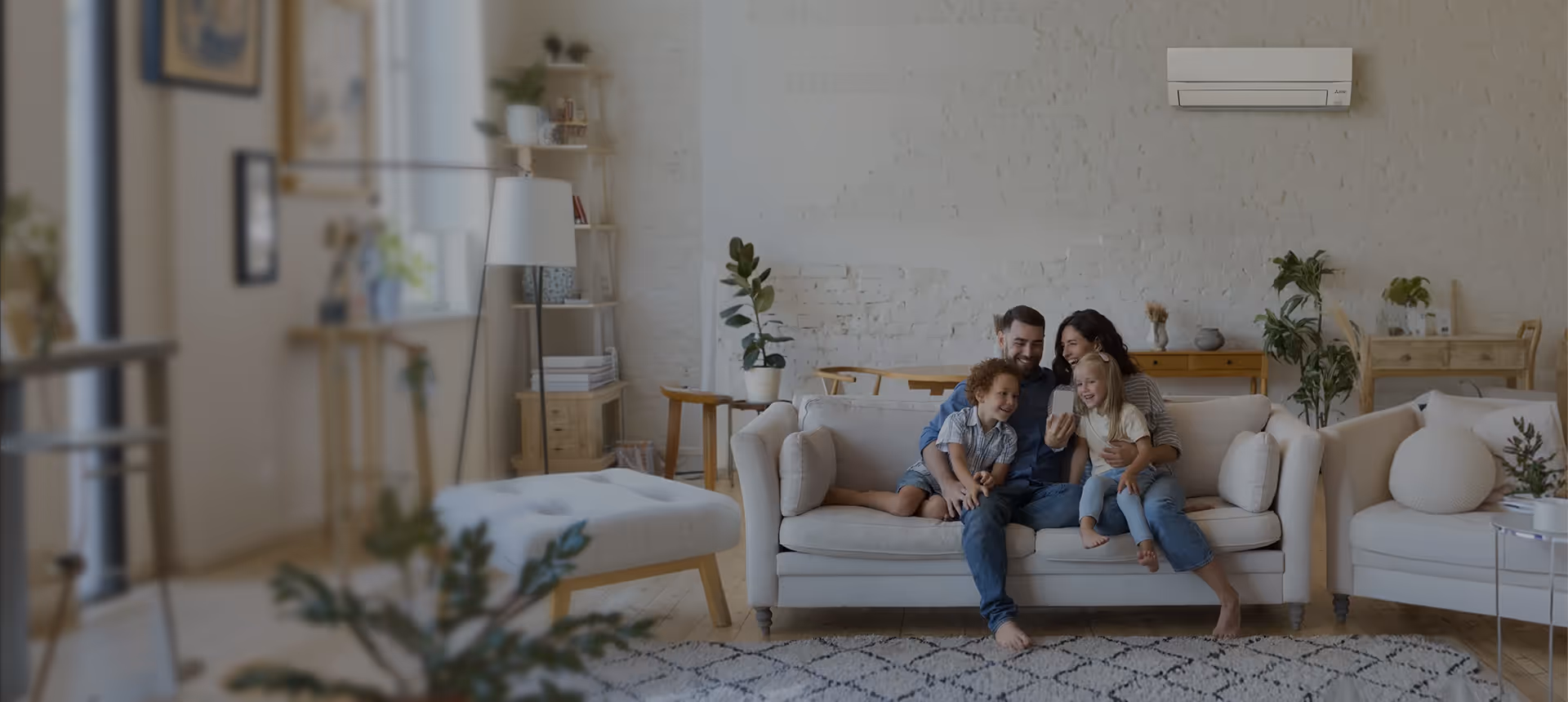 Une famille heureuse de deux adultes et deux enfants assis sur un canapé dans un salon lumineux avec un climatiseur mural.