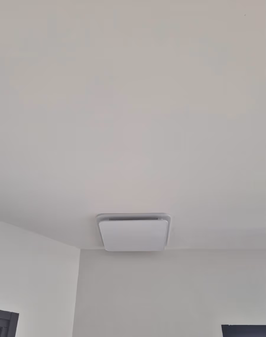 Unité de climatisation gainable carrée montée au plafond blanc d'une pièce.