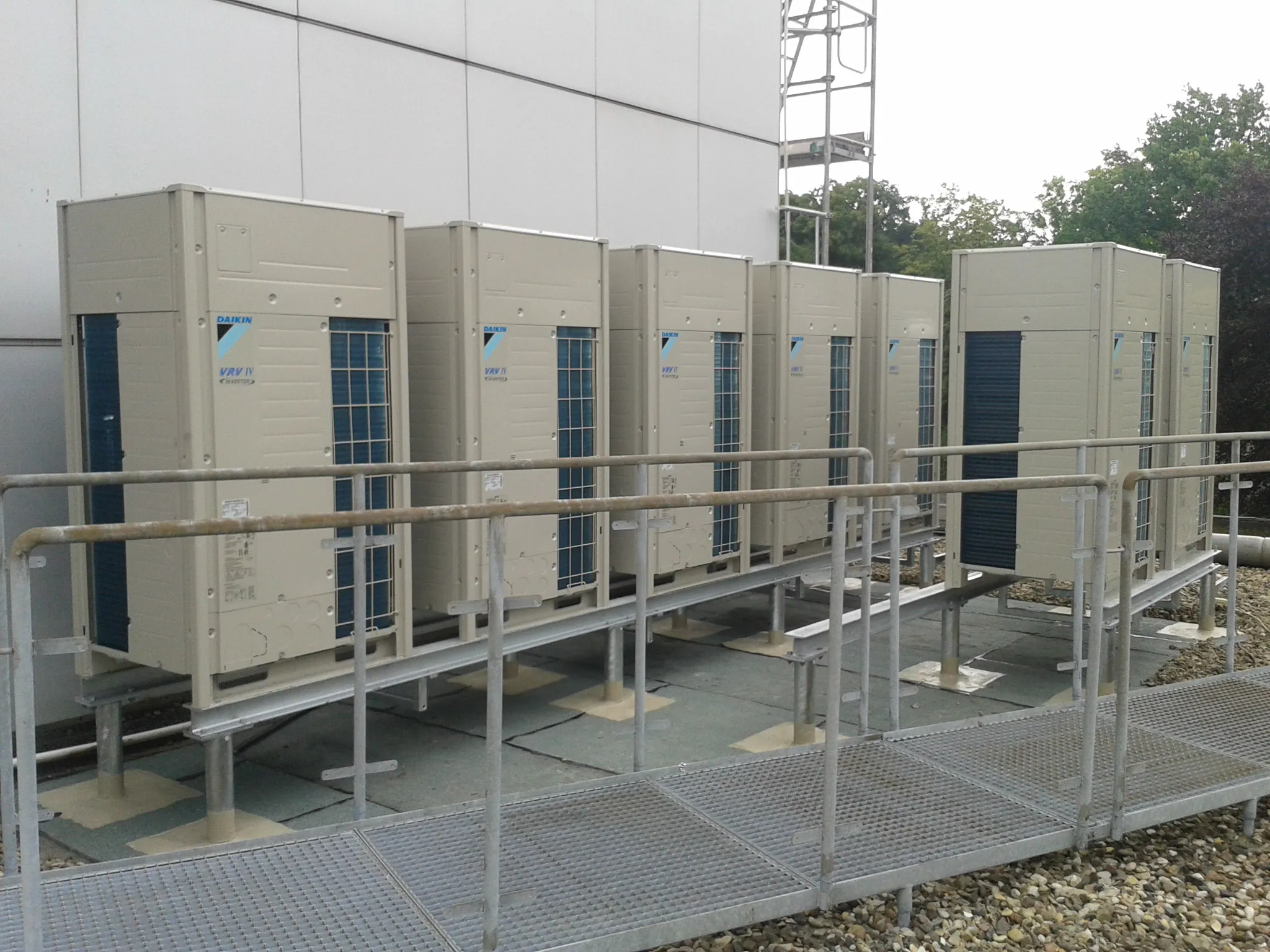 Mehrere große Daikin VRV IV Klimaanlagen auf einem Metallständer vor einem Gebäude.
