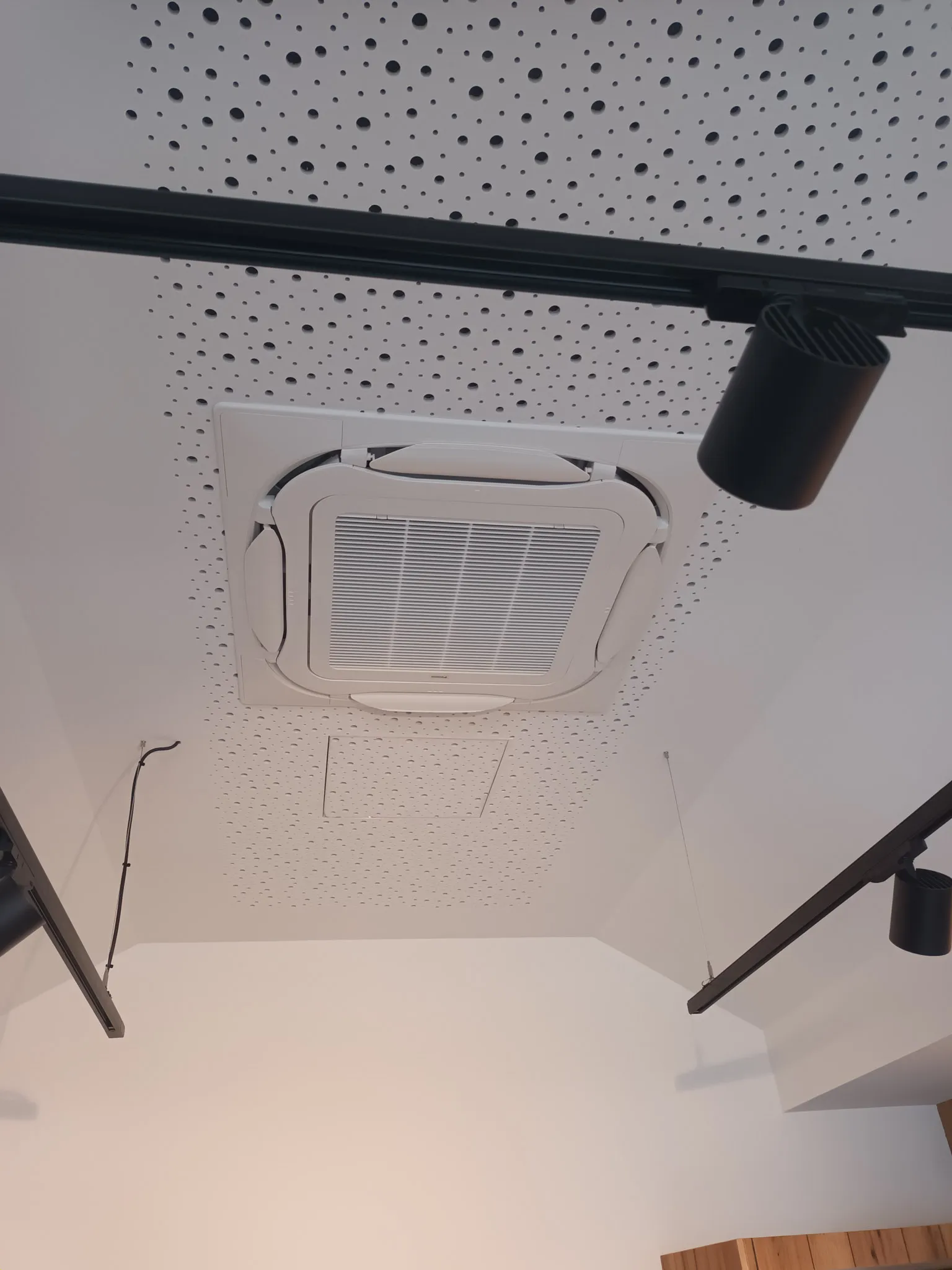 Decke mit integrierter Klimaanlage und schwarzen Spotlight-Schienen in einem modernen Raum.