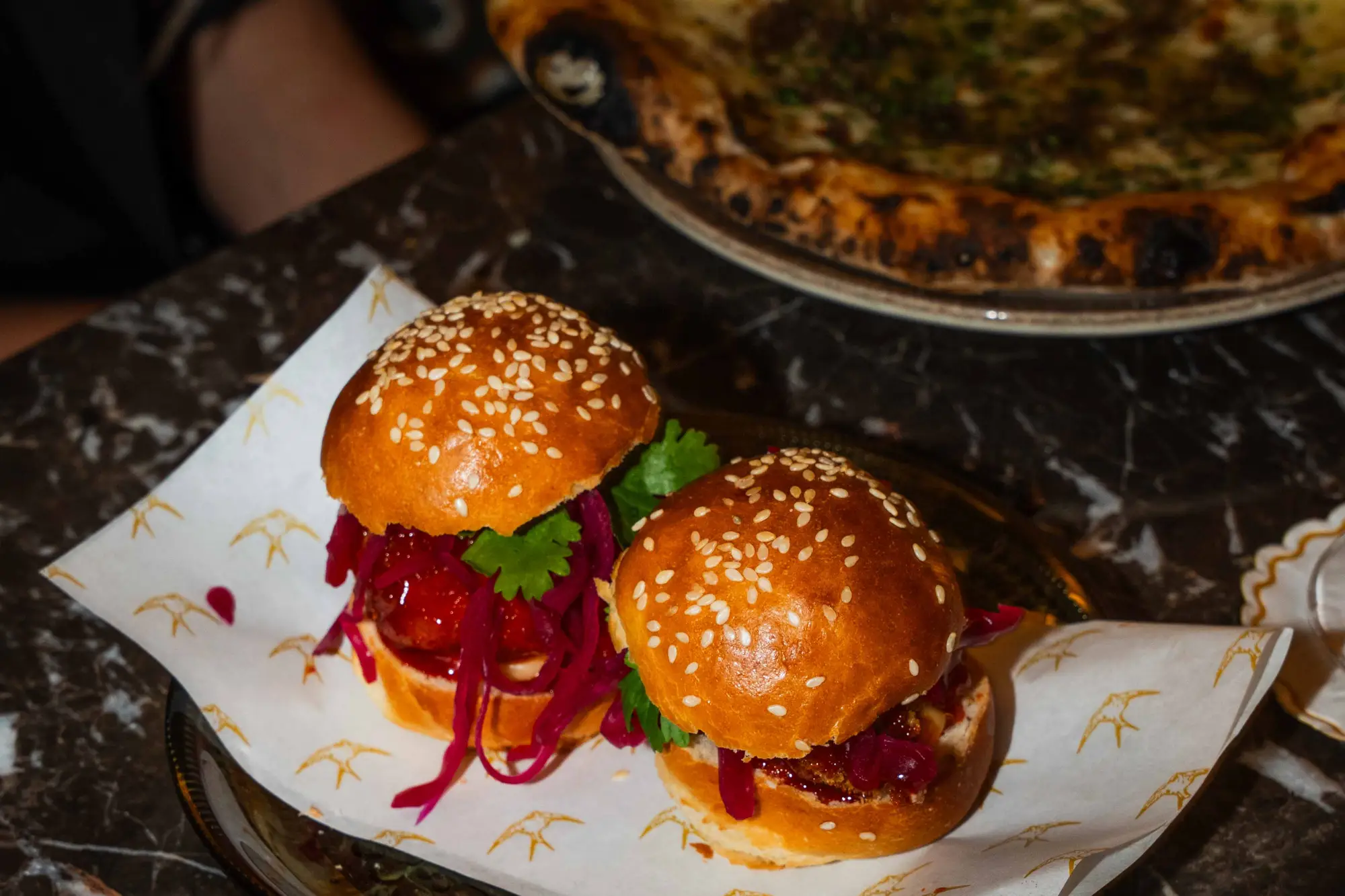 Två små hamburgare med sesamfröbröd, rödbetssallad och koriander serverade på ett papper.