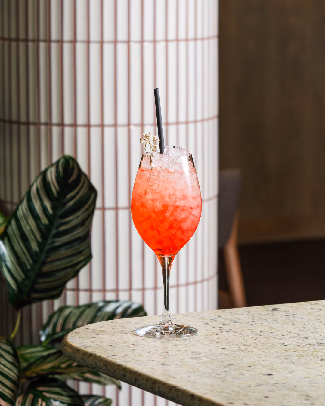 Röd iskall cocktail i vinglas med svart sugrör och liten vit blomdekor, placerad på marmorbord.