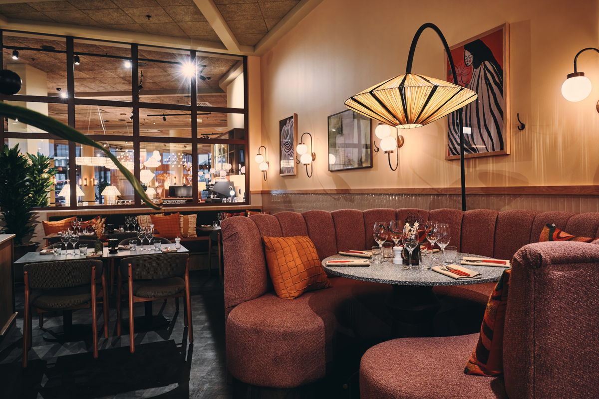 Mysig restauranginteriör med rund, röd soffa runt ett bord, elegant belysning och konst på väggarna.