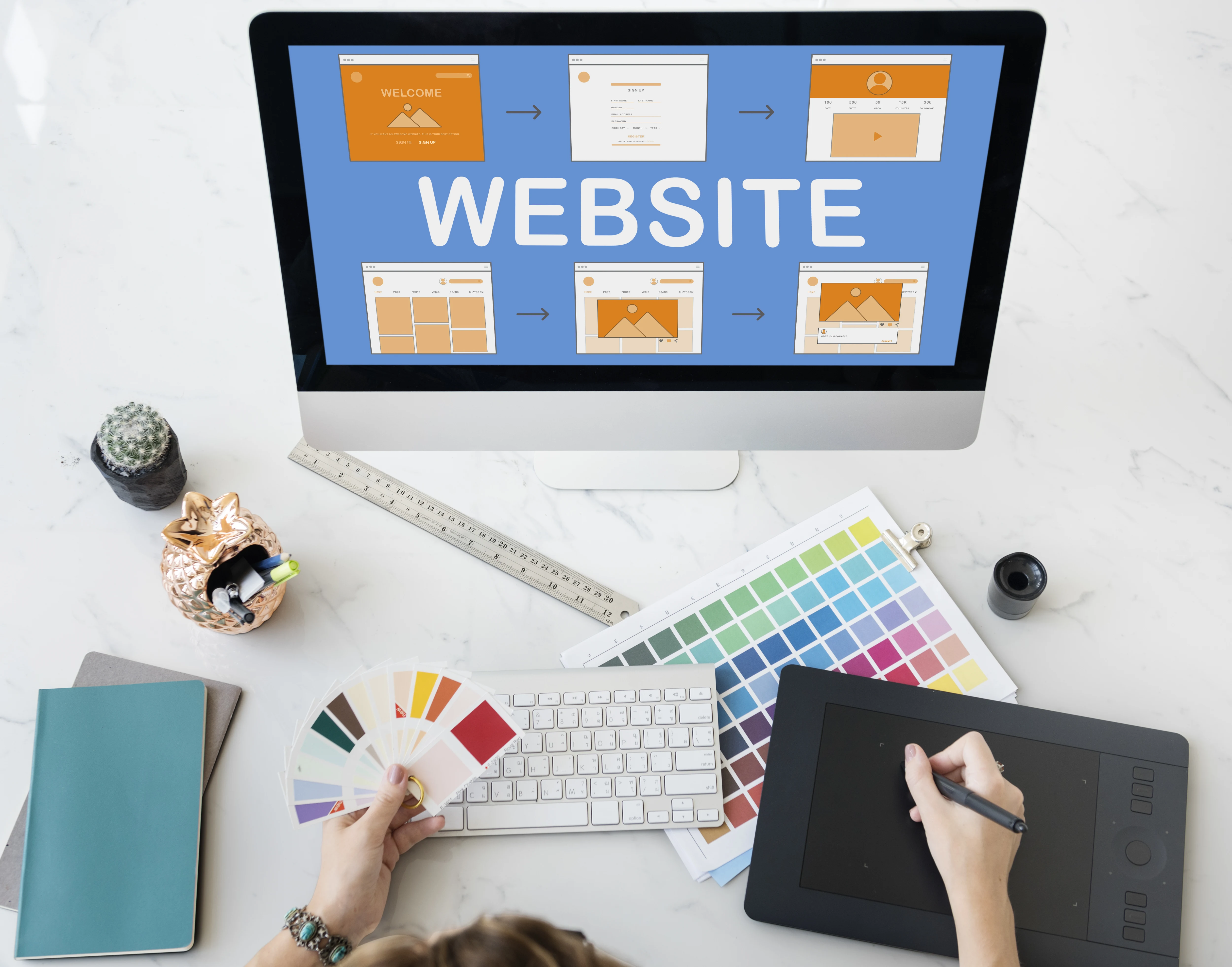 Web designer working on website redesign with color swatches, graphics tablet, and layout on computer screen.