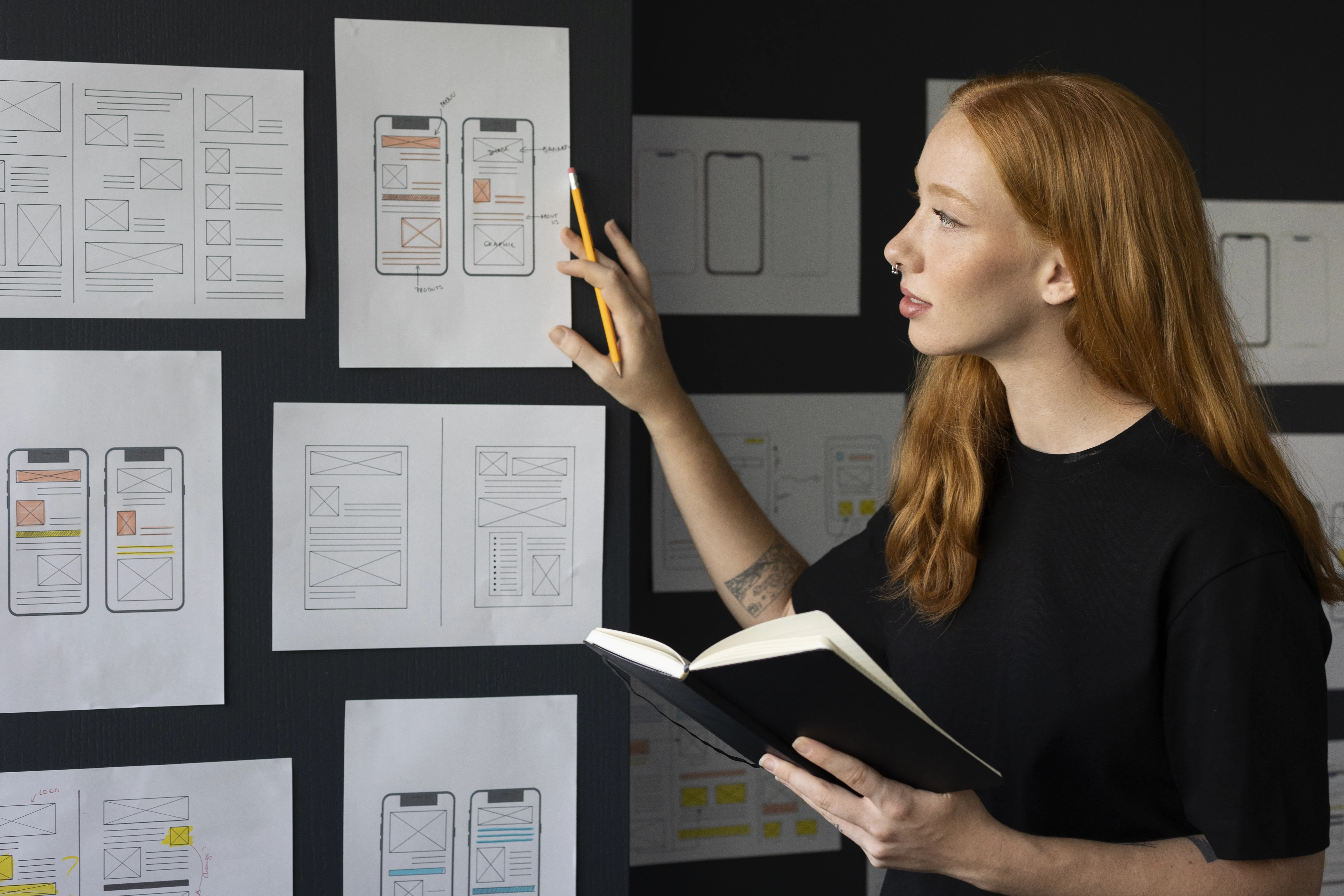 Designer reviewing wireframes and sketches for UX Audit Services, holding a notebook and pencil in a creative workspace.