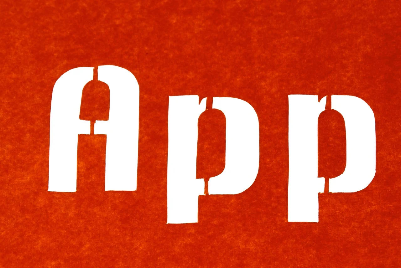 Bold white "App" text cutout on a textured red background, symbolizing app development and mobile technology concepts.