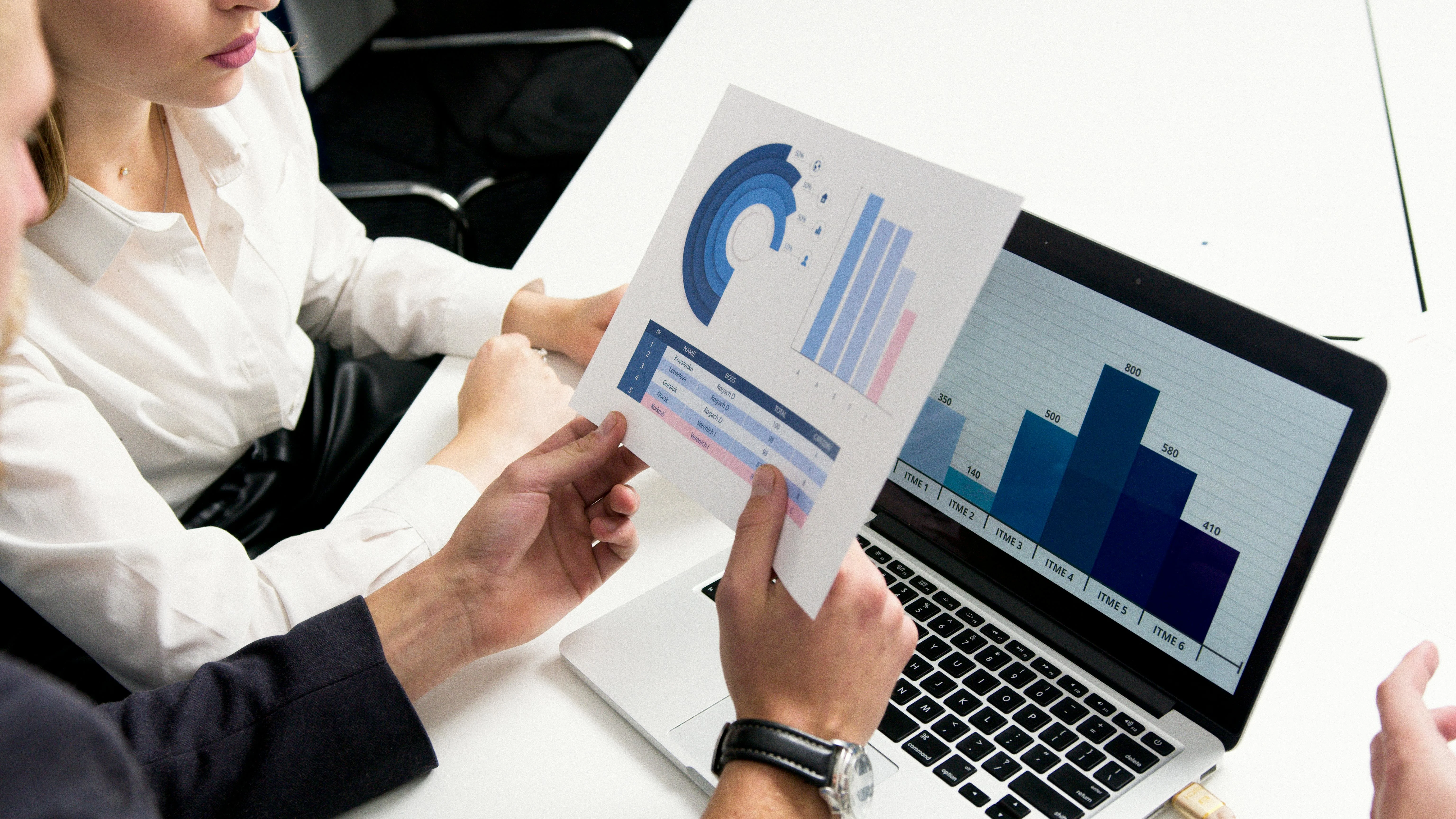 Business team analyzing UX Competitive Analysis data with charts and graphs on paper and laptop screen, showcasing data-driven decision-making in a professional office setting.