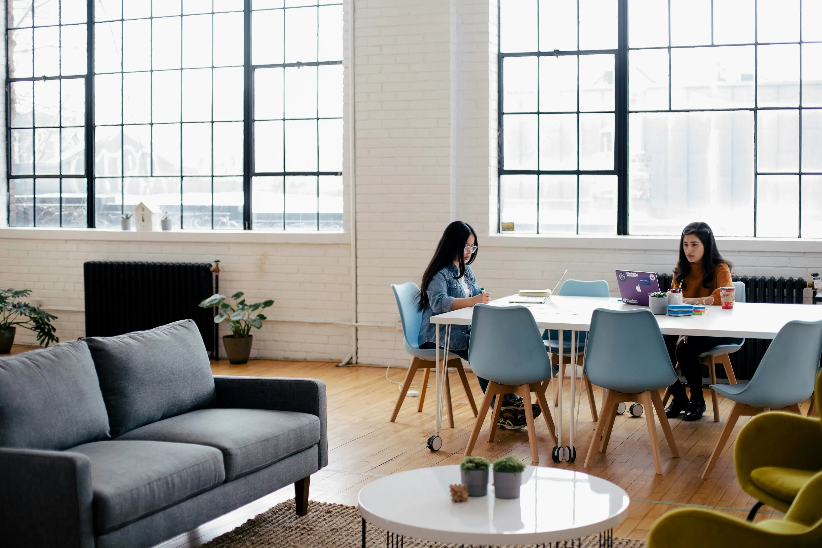 Two women working in a modern coworking space, collaborating on UX consultant projects with laptops.