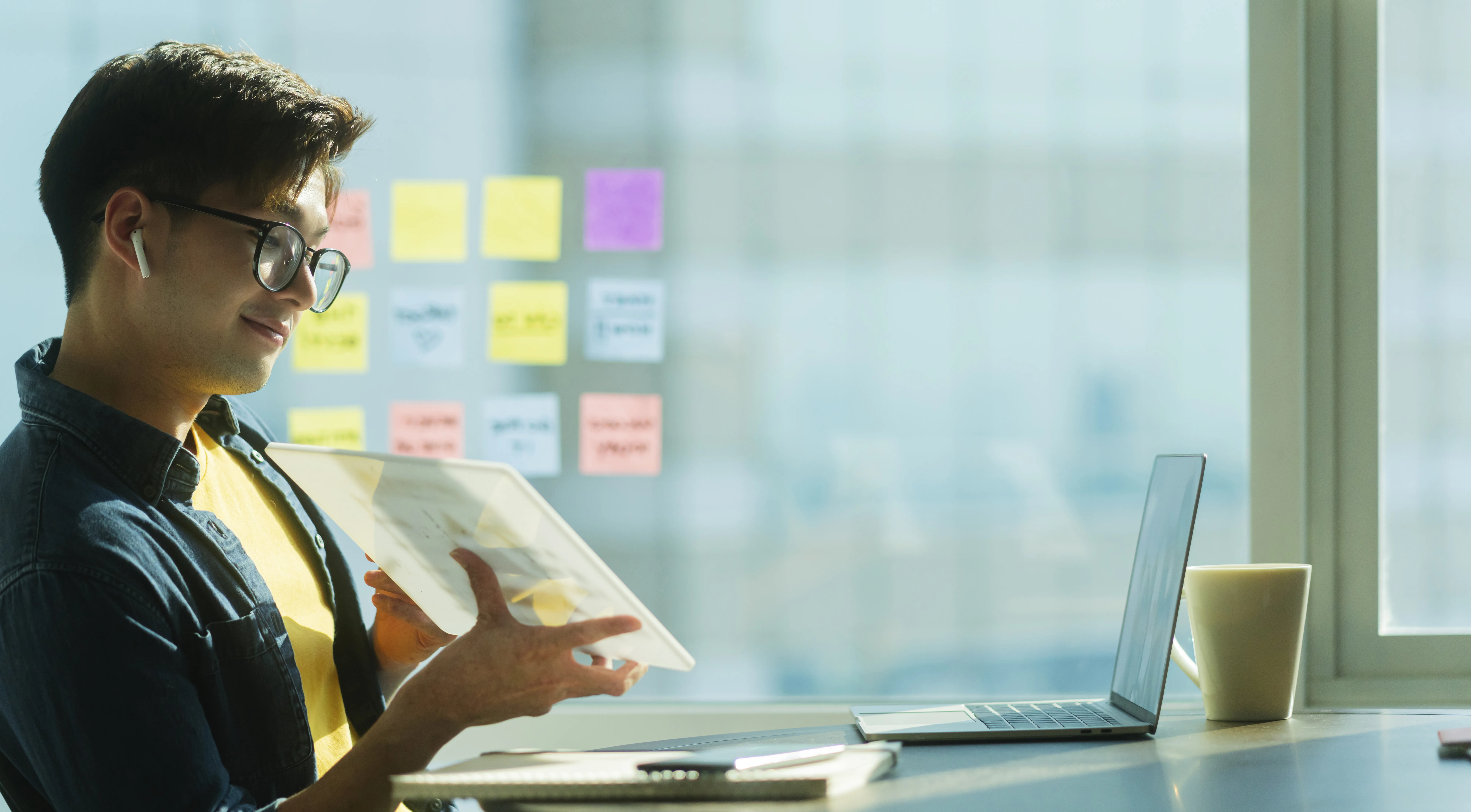 UX Researcher reviewing documents at a desk with laptop, coffee cup, and sticky notes on a windowed office background, highlighting modern research workflow.