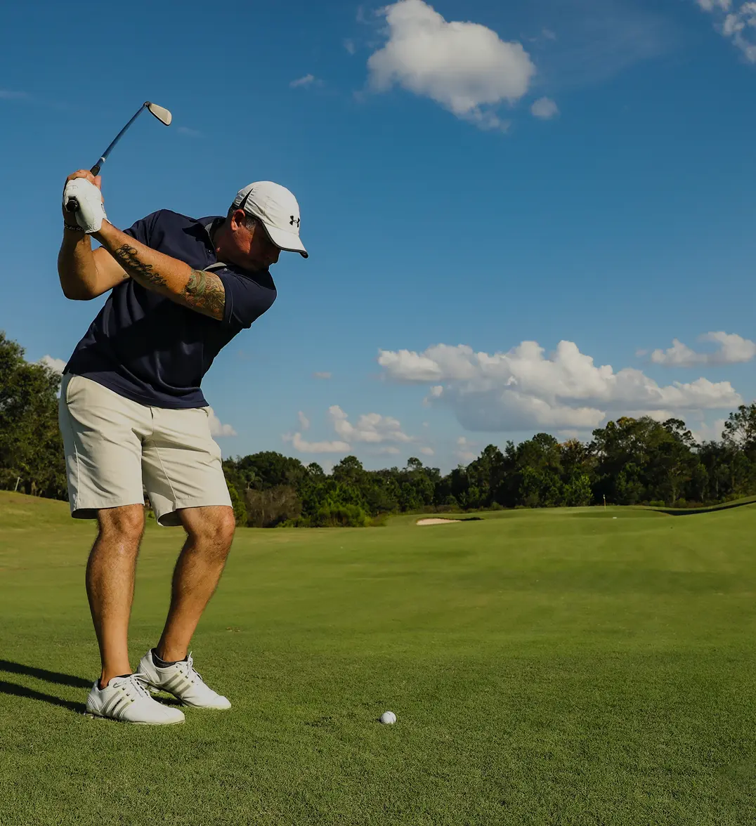 A golfer mid-swing on a green golf course with a clear blue sky in the background, with the Wedge Guys logo in the top right corner