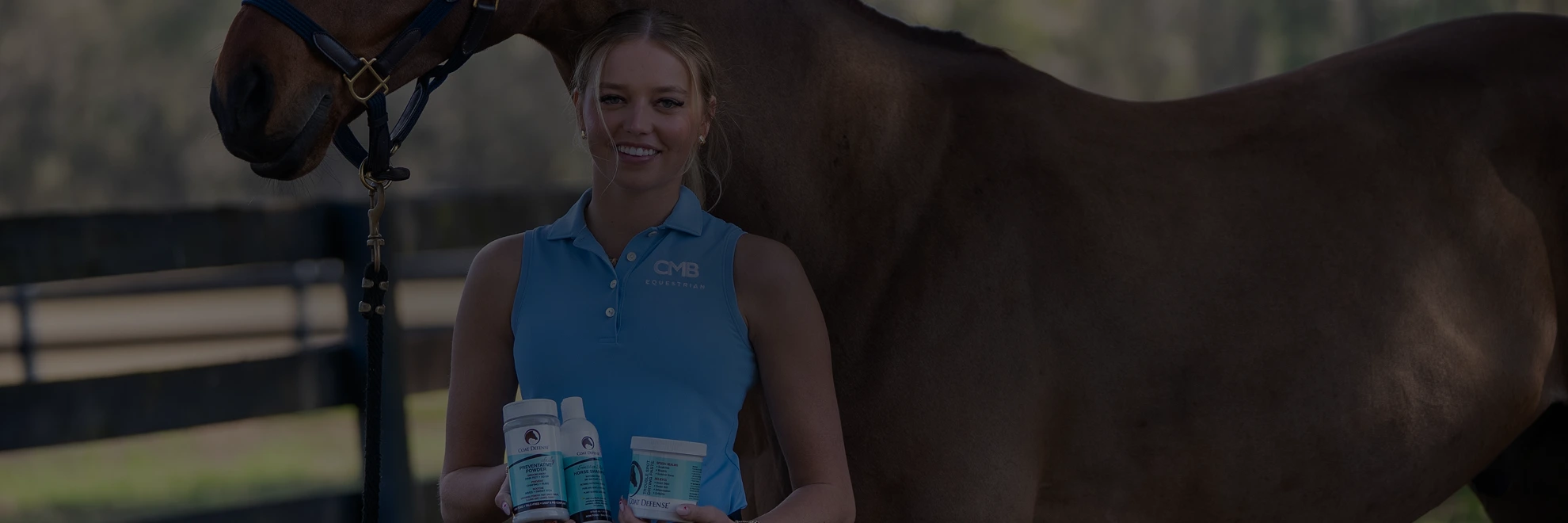 Woman in blue polo holding Coat Defense next to a brown horse in a paddock