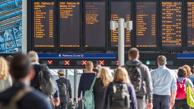 Photo d'une foule nombreuse consultant les panneaux d'affichage des départs dans une gare très fréquentée