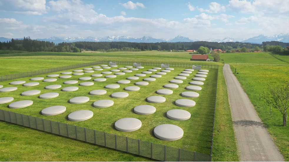 Field of Qnetic flywheel storage units integrated into a grassy landscape with mountains in the background.