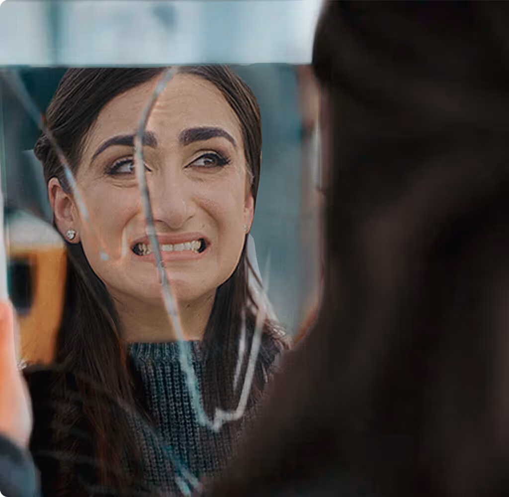 Steph mira su reflejo en un espejo roto, con una expresión de dolor o frustración.