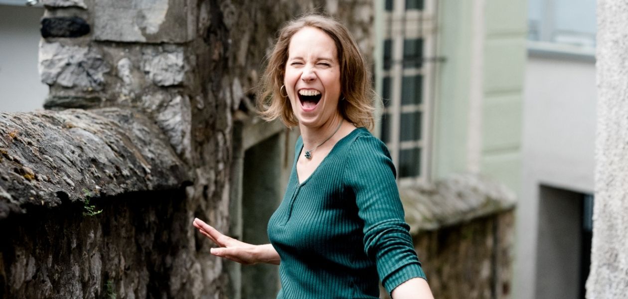 Eine Frau in einem grünen Pullover die explosiv in die Kamera lacht