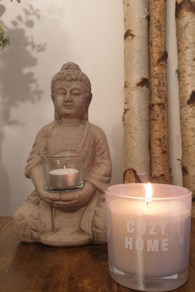Eine brennende Kerze im Vordergrund und ein Buddha im Hintergrund