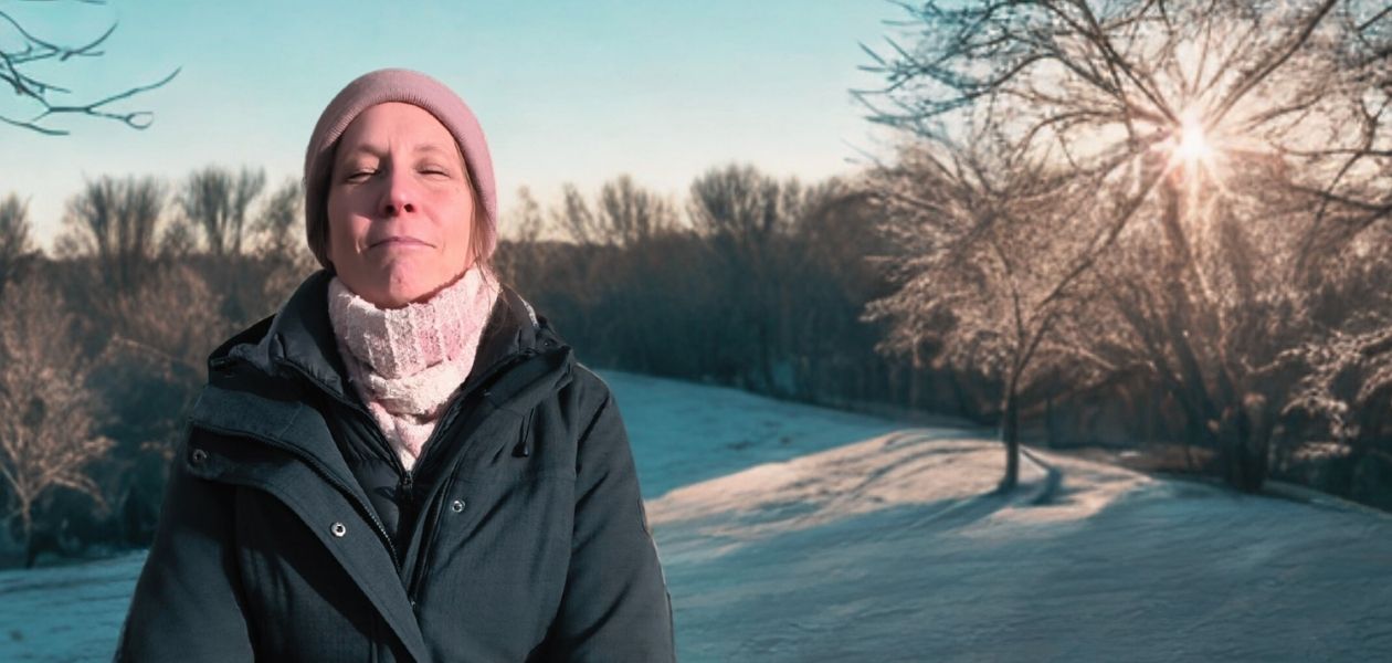 Eine Frau am linken Bildrand geniesst mit geschlossenen Augen die Sonne in einer Winterlandschaft
