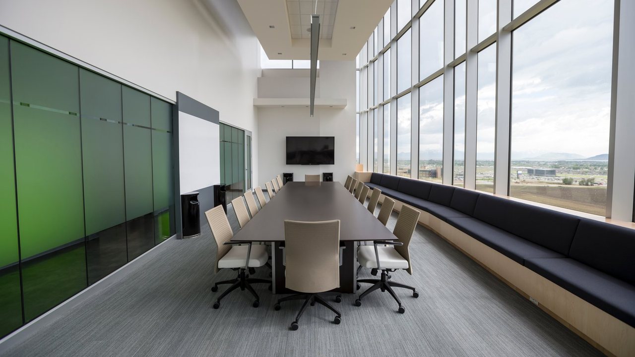 A long boardroom table with chairs beside a glass wall