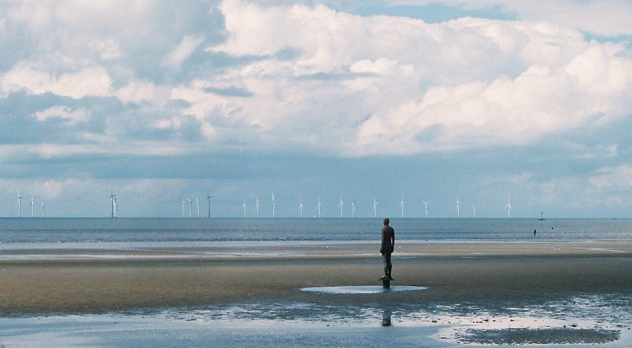 Offshore wind turbines on the horizon seen from a wide sandy beach