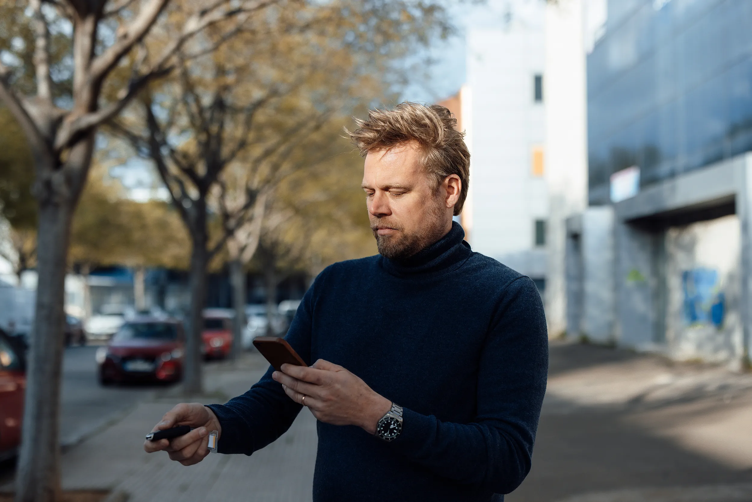man looking at a smartphone and opening the car with his key
