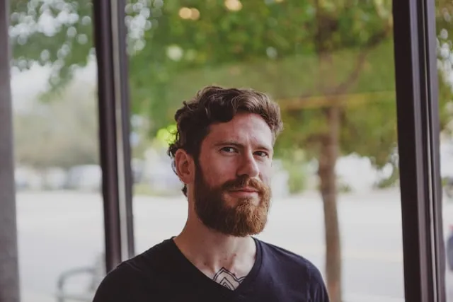 A man with a beard standing in front of a window.