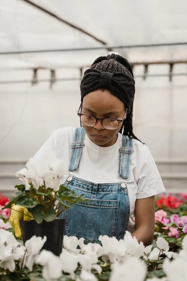 A woman in overalls and glasses working in a greenhouse.