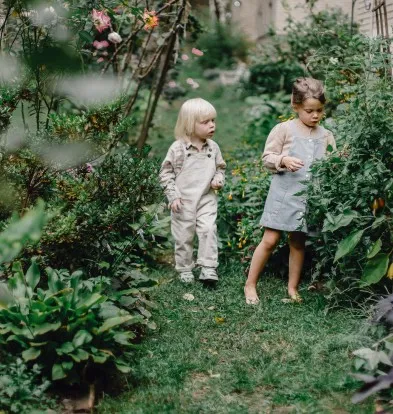 Two little girls are standing in a garden.