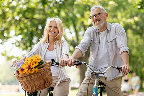 An older man and woman ride bicycles in a park, pain free and smiling.