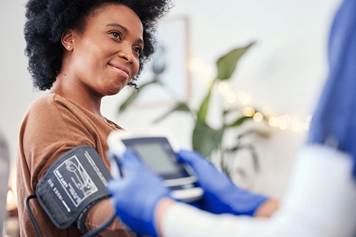 A woman is smiling as she has her blood pressure taken by a doctor in an outpatient setting, using a cuff on her arm.