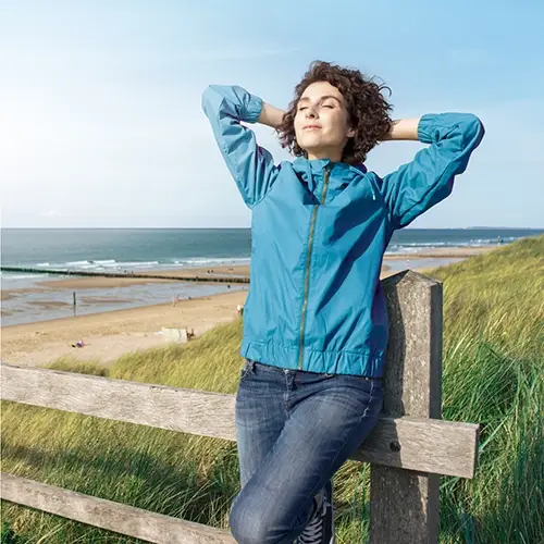 A woman is standing on the beach, relaxed and free from back pain and enjoying the sun with her eyes closed.