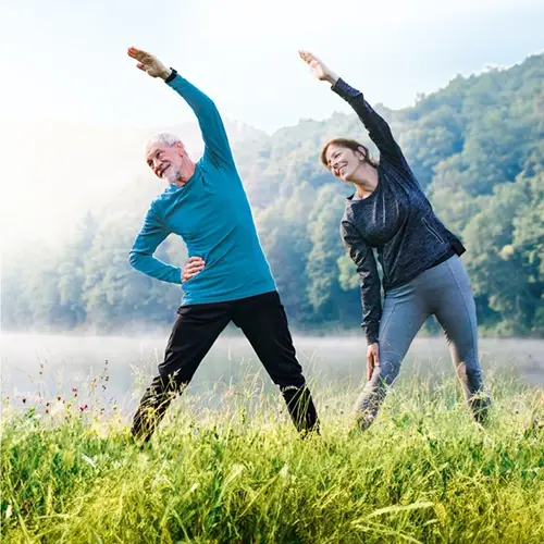 An older man and woman are doing stretching exercises in a meadow.