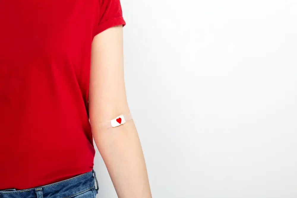 View of part of the body of a young woman in a red t-shirt with a plaster in the crook of her elbow after giving a blood sample.