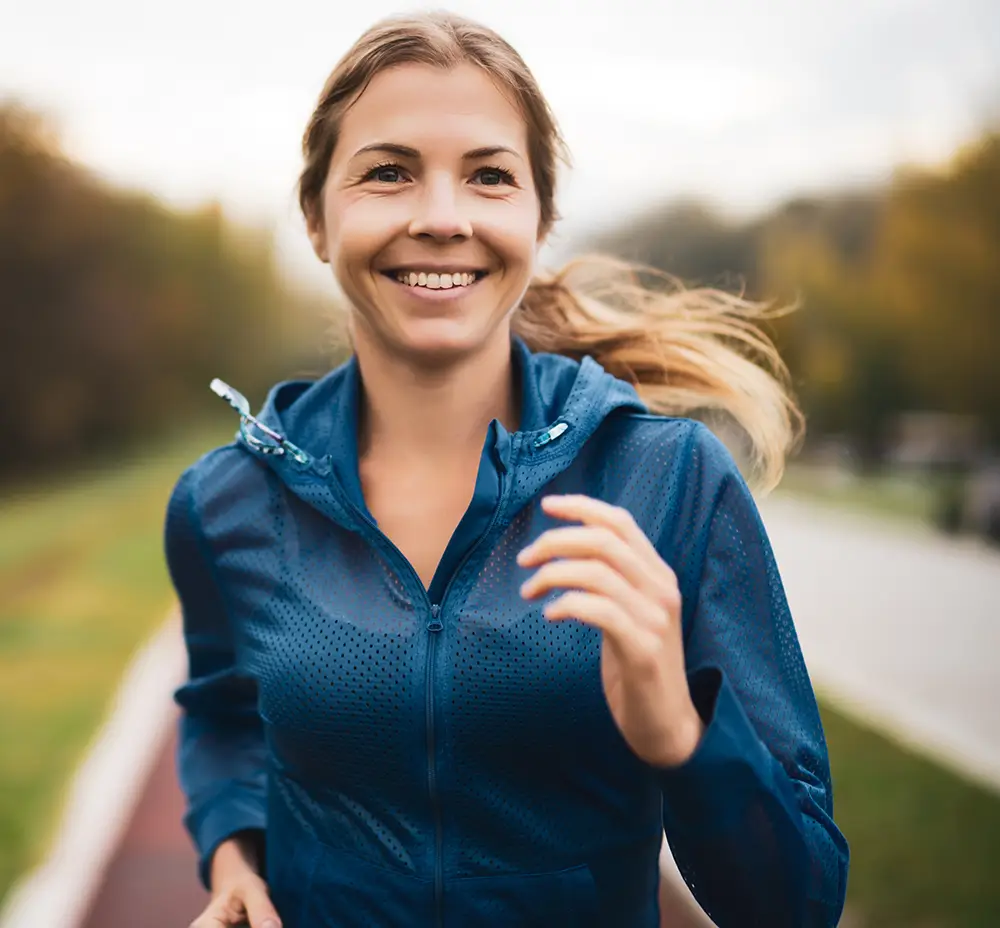 A young jogger is laughing while running surrounded by nature.