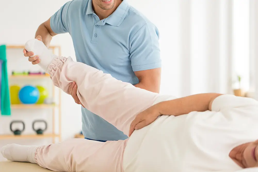 A physiotherapist helps an older woman with stretching exercises.