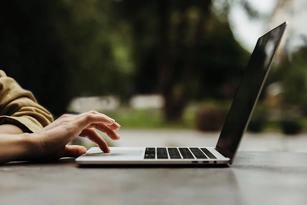 A woman works on a laptop while sitting outside.