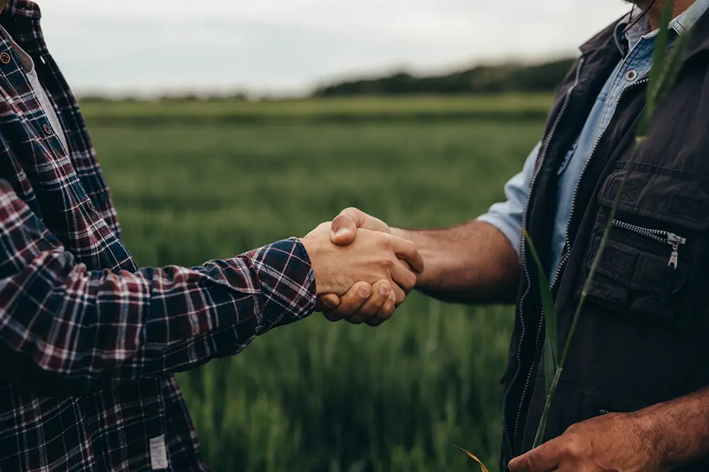 Two men shake hands vigorously surrounded by nature.