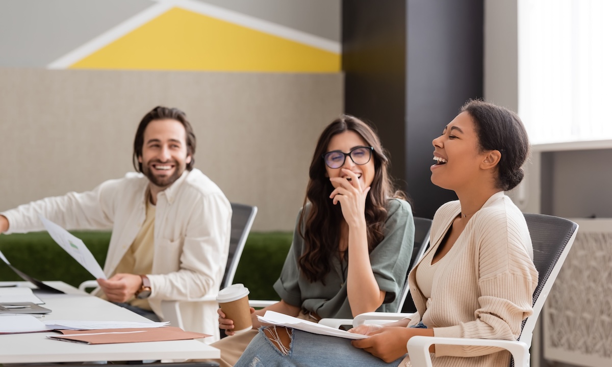 Groupe de collègues assis autour d’une table lors d’une réunion informelle, échangeant dans une atmosphère détendue et conviviale, illustrant la collaboration et le bien-être au travail.