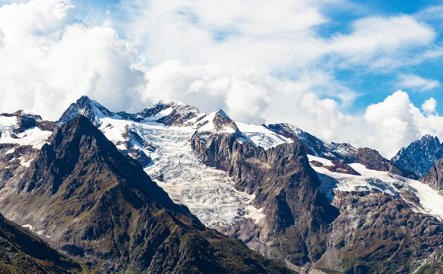 Snowy mountain peaks with glaciers under fluffy white clouds