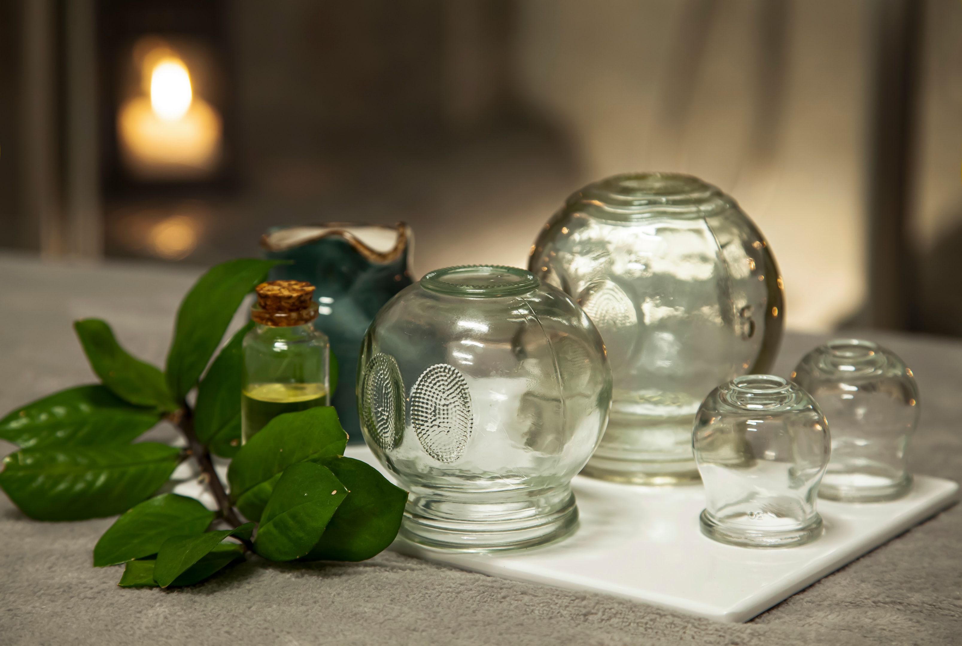 Various glass cupping cups arranged on white tray with green plant and oil bottle in spa setting