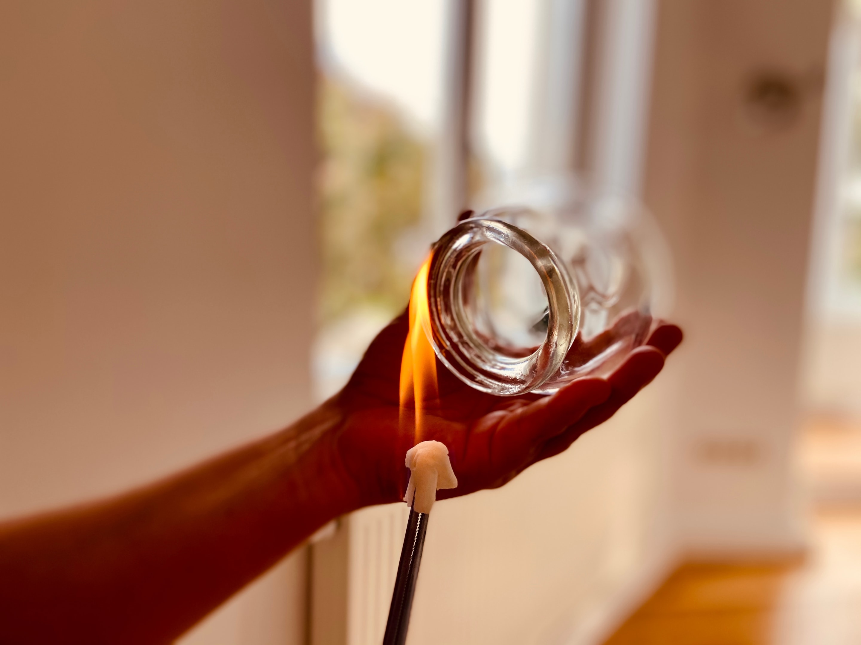 Hand holding glass cupping cup with flame from lighter creating suction for cupping therapy