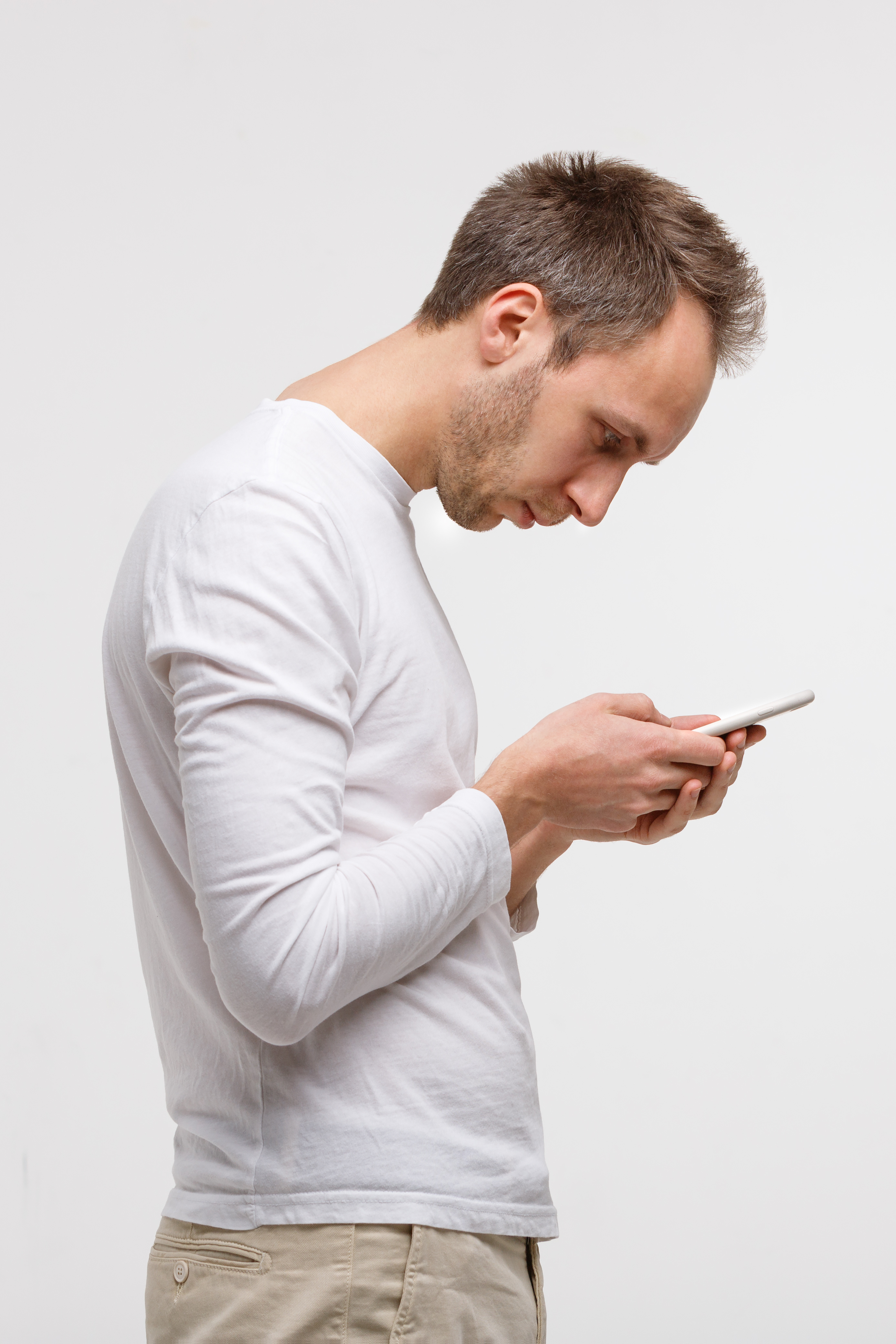 Man in white long-sleeve shirt looking down at smartphone against white background