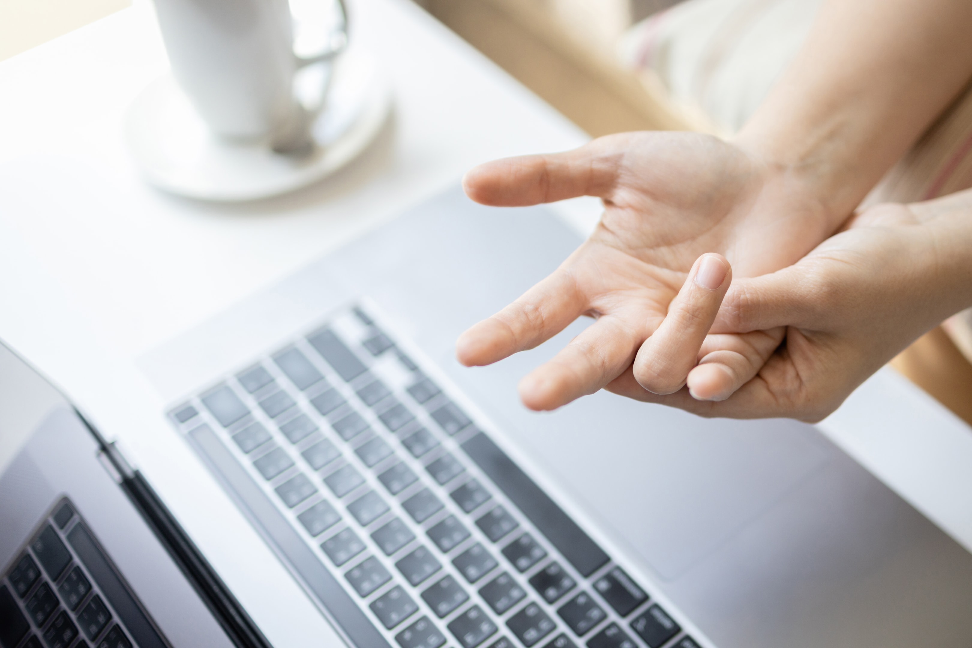 Person stretching hands and fingers above laptop keyboard, appearing to have wrist or hand strain